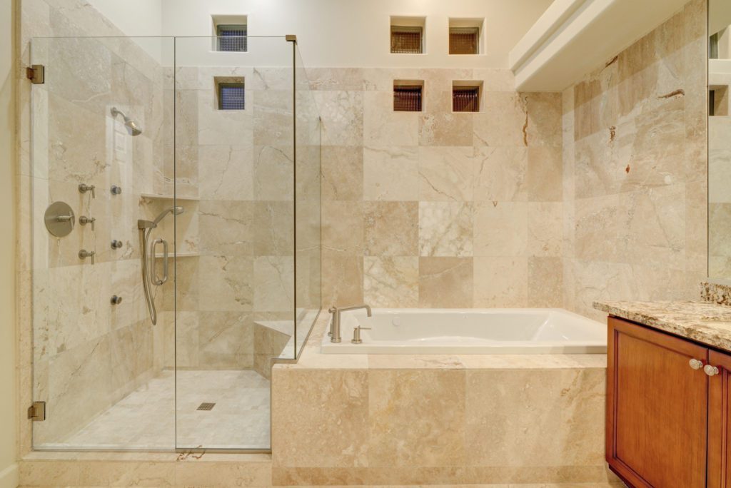 A bathroom with marble tile and glass shower door.