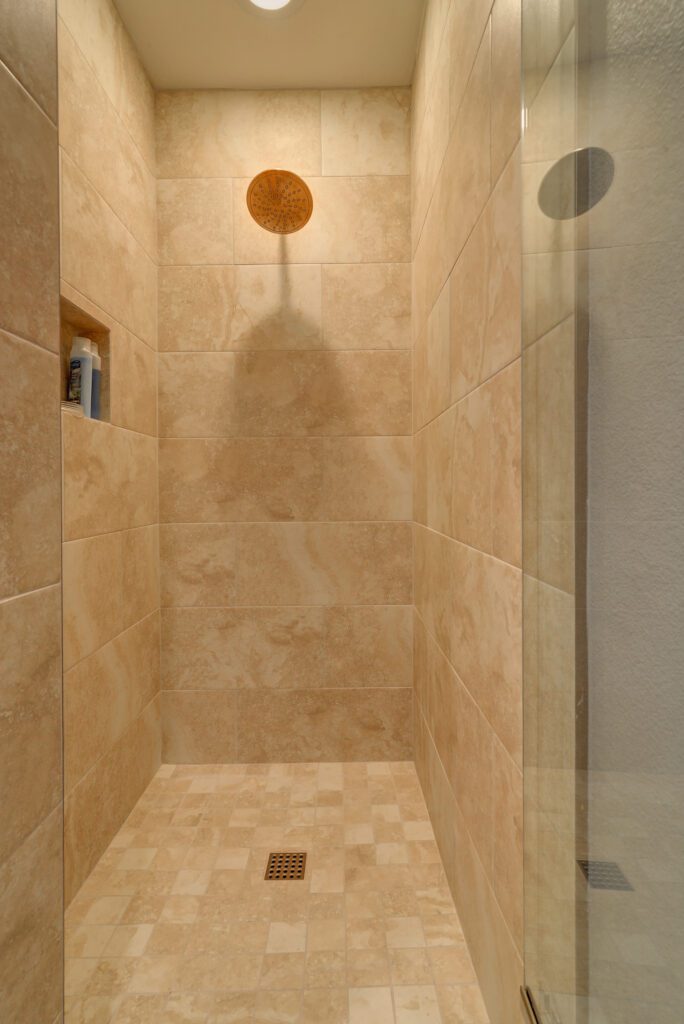 A shower with beige tile and a glass door.