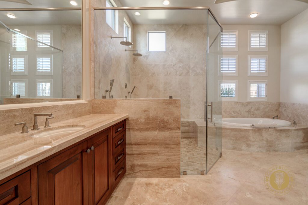 A bathroom with marble walls and floors, and a glass shower door.