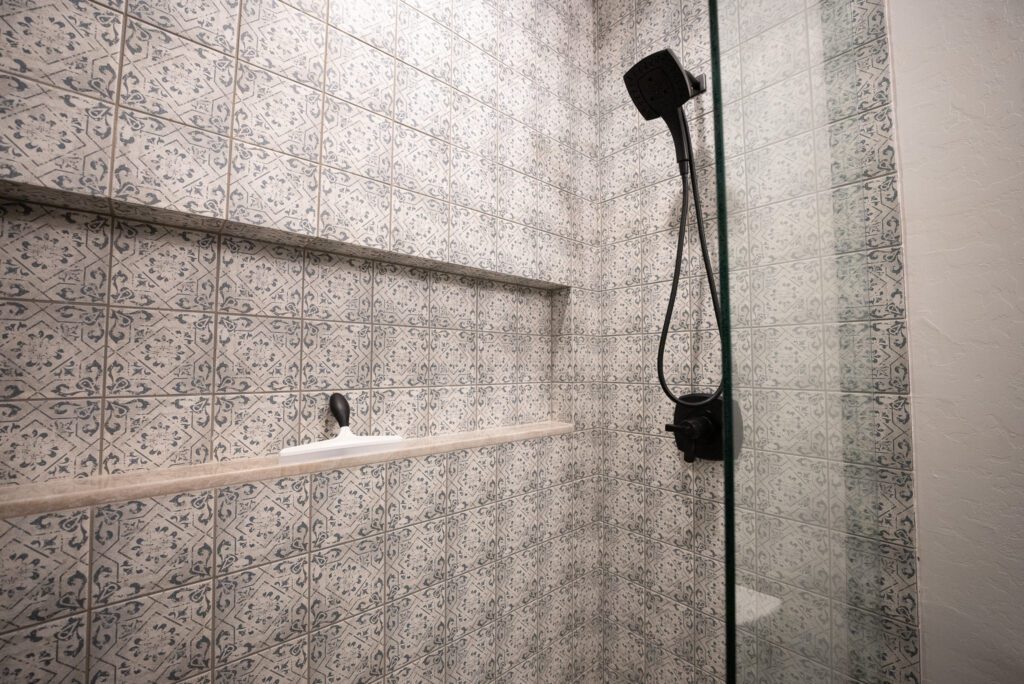 A shower with a glass door and tiled walls.
