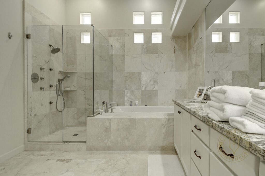 A bathroom with marble walls and floors, a tub, shower and sink.